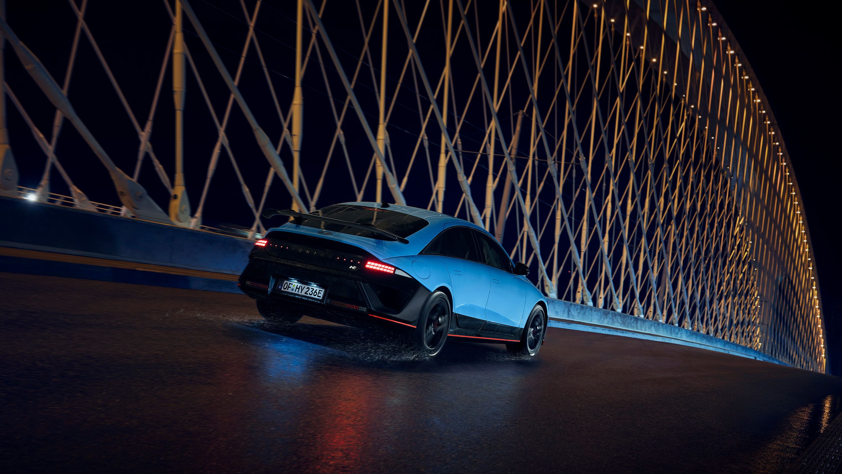 Hyundai IONIQ 6 N egy híd alatt halad el éjszaka, körülötte megvilágított építészeti elemek.