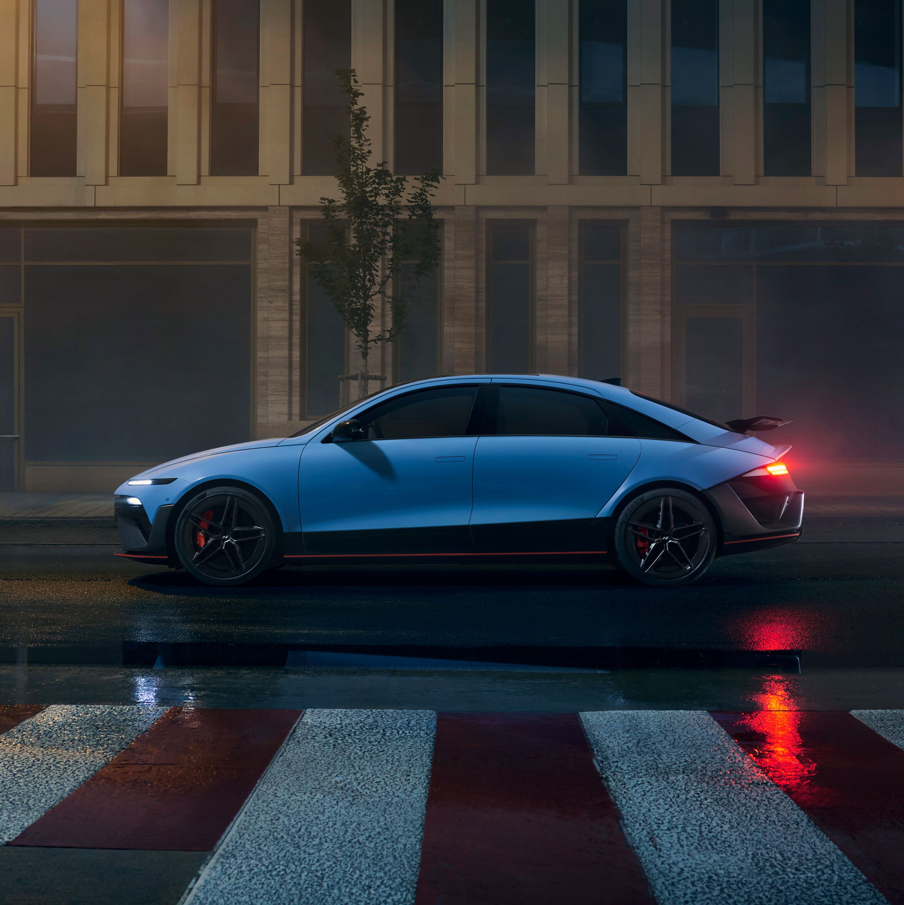 Hyundai IONIQ 6 N éjszaka a városban parkol, a vizes aszfalton tükröződnek a város fényei. Oldalnézetből.